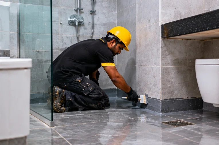 Technician sealing bathroom floor and wall joints to prevent water leakage
